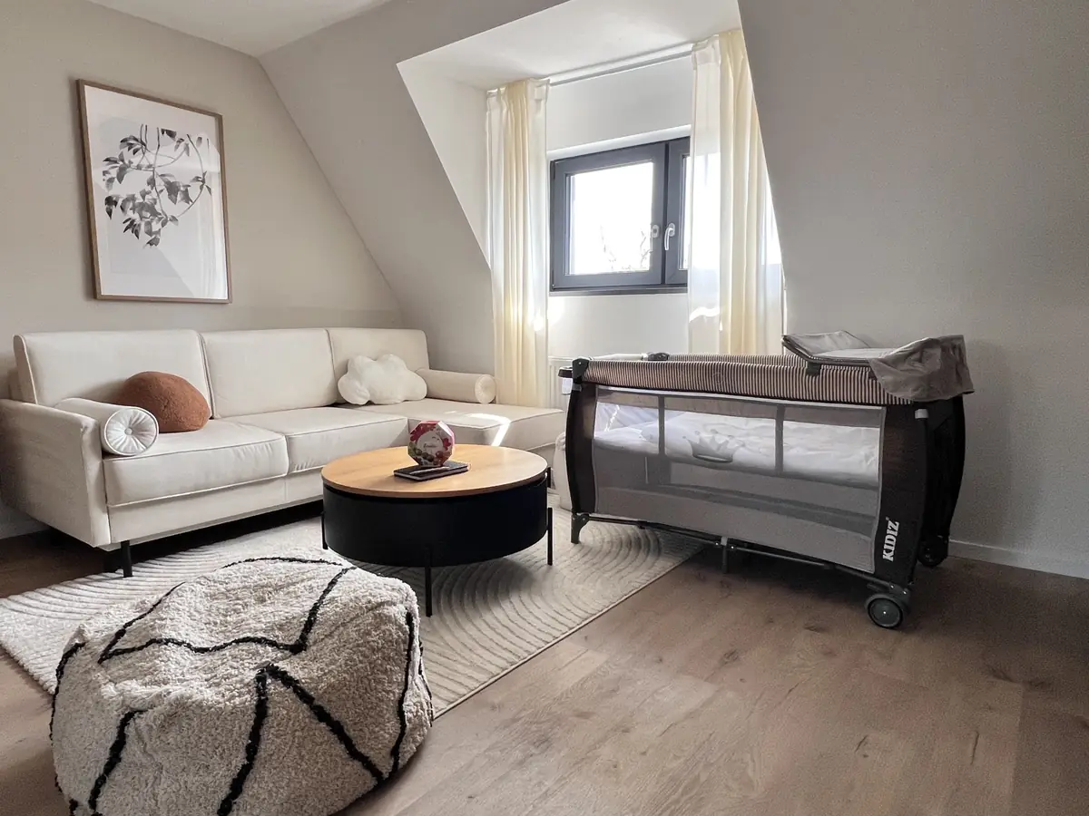 Aufgebautes Reisebett neben hellem Sofa im Wohnbereich, Raum mit Dachschräge