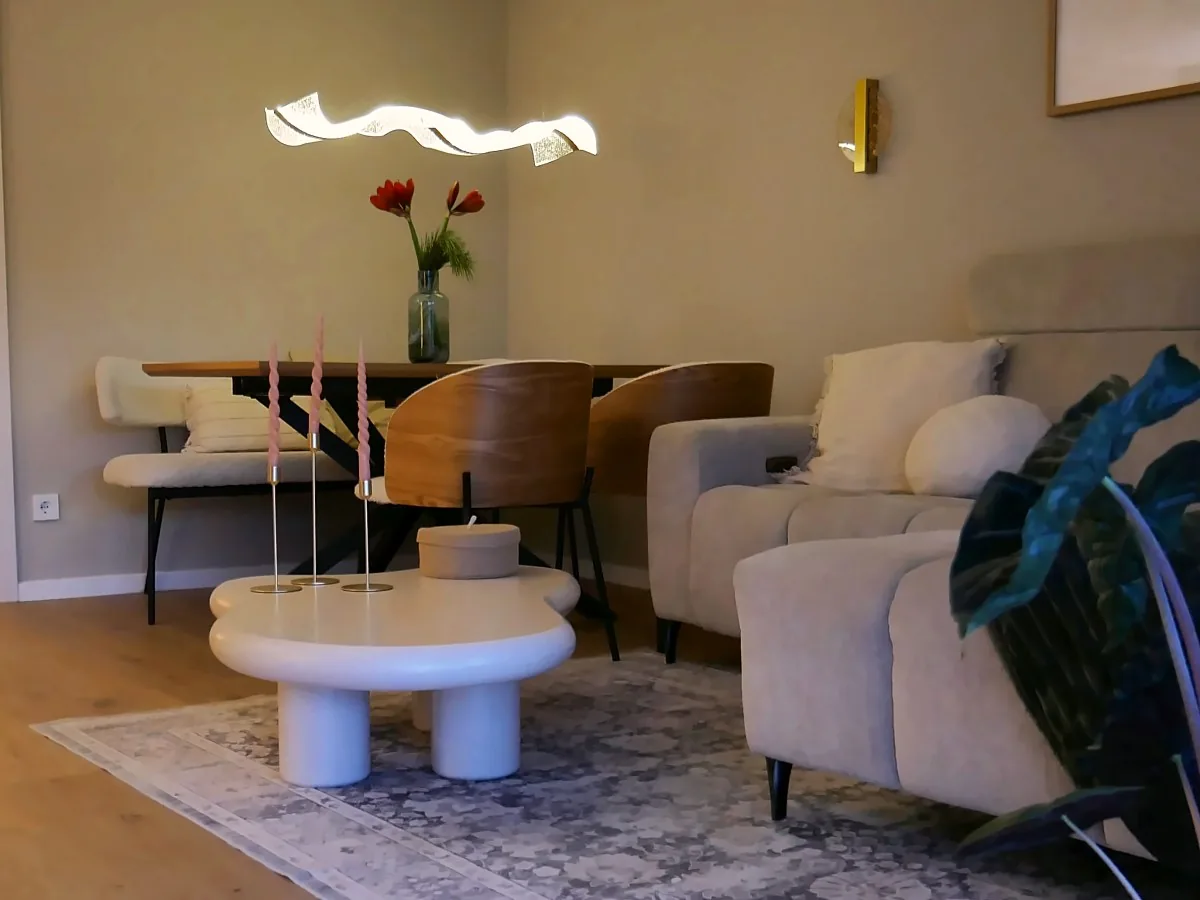Esstisch mit Bank und Stühlen am Abend, darüber die Leuchte, auf dem Tisch eine Vase mit roter Amaryllis, vorne Sofa und Couchtisch mit Kerzen