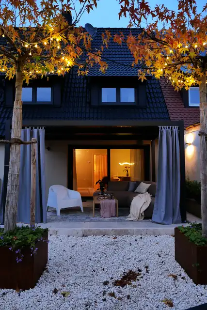 Die WolkenGuckerei am Abend, Terrasse beleuchtet, davor ein Baum im Herbstlaub