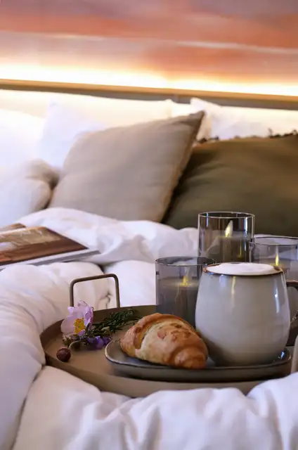 Frühstückstablett mit Croissant und Kerzen auf dem Bett