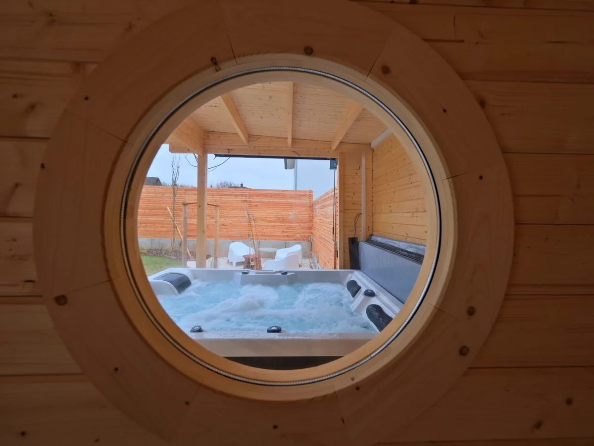 Blick aus der Sauna durch das runde Fenster auf den Whirlpool