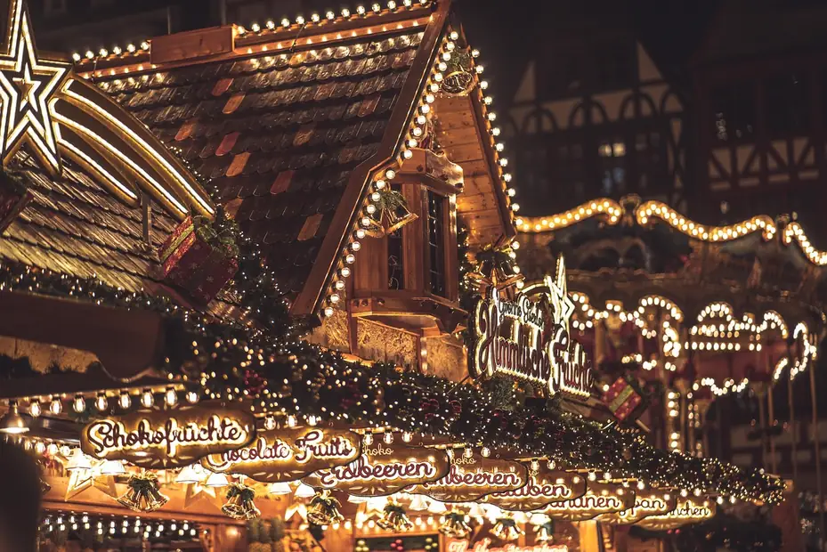 Reich beleuchtete Weihnachtsmarktbude mit Lichterketten und Karussell im Hintergrund