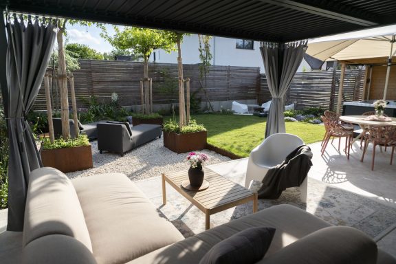 Wohnzimmer draußen Gepflegte Gartenlandschaft mit Möbeln und Pflanzen unter einem Überdach.