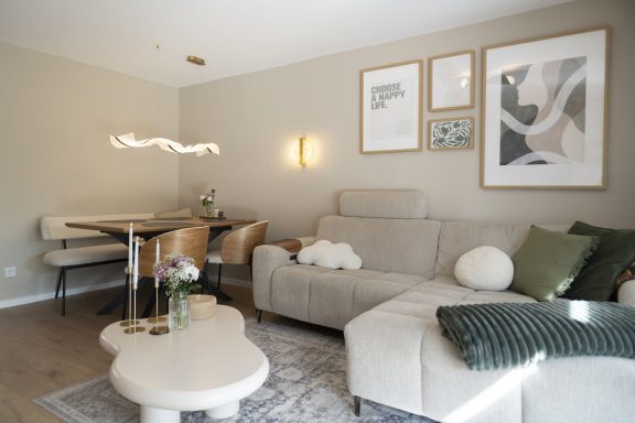 Helles Wohnzimmer mit gemütlicher Couch, Esstisch und dekorativen Bildern an der Wand.