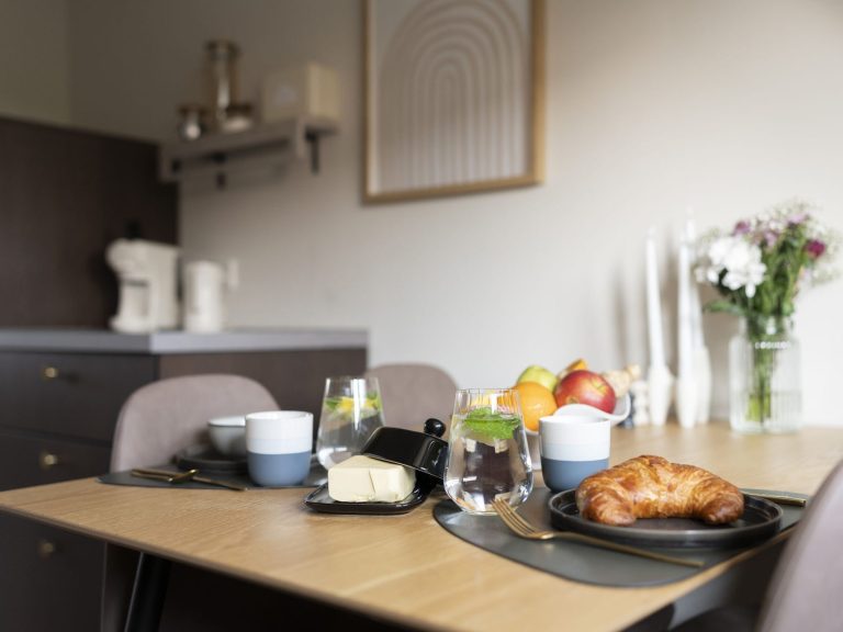 Frühstückstisch Frühstückstisch mit Croissant, Obst, Joghurt und Blumenarrangement in modernem Ambiente.