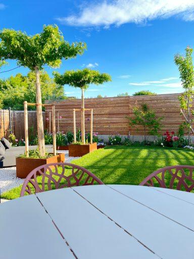 Gartenlandschaft mit Bäume, Rasenfläche, Tisch und Sonnenschein.
