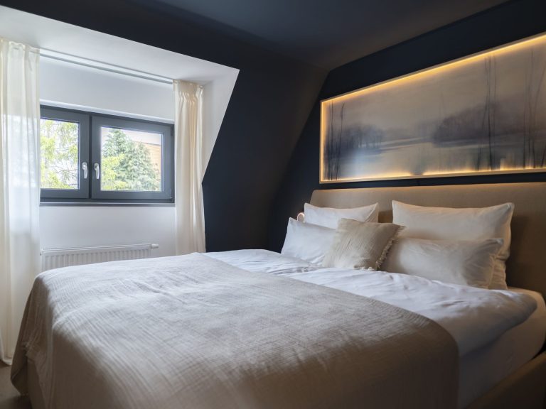 Schlafzimmer WolkenBlick Ein helles Schlafzimmer mit einem Bett, auf dem eine beigefarbene Decke liegt.