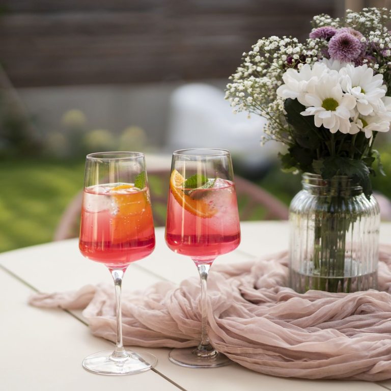 Aperol Time Zwei Cocktails mit Früchten und Eiswürfeln, daneben eine Blumentopf mit weißen Blumen.