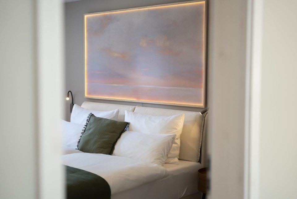 Bett mit beleuchtetem Sonnenuntergangs-Bild darüber