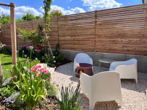Heller Gartenbereich mit weißen Stühlen, Tisch und bunten Blumen.