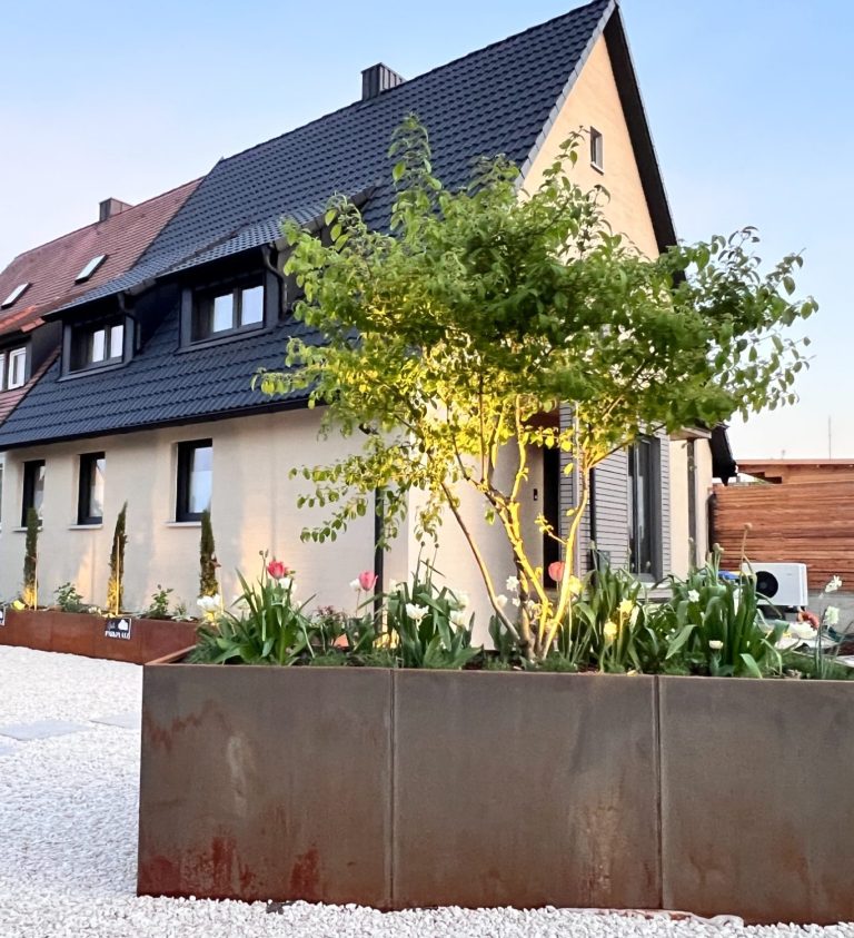 Modernes, zweistöckiges Haus mit schwarzem Dach und freiem Vorplatz.