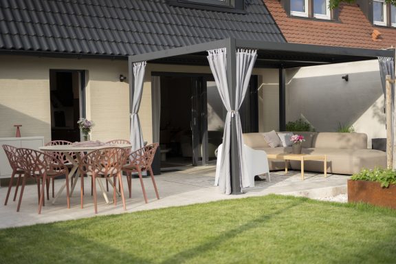 Veranda Gartenbereich mit Möbeln, Tisch und Pergola auf einer gepflasterten Terrasse.