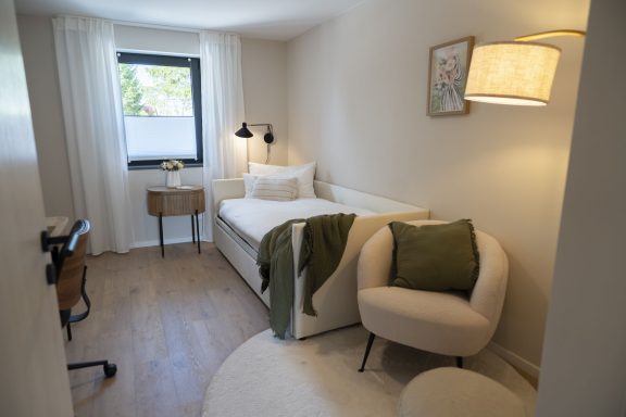 2. Schlafzimmer Helles Zimmer mit Einzelbett, einem Sessel, Tisch und sanften Farbtönen.