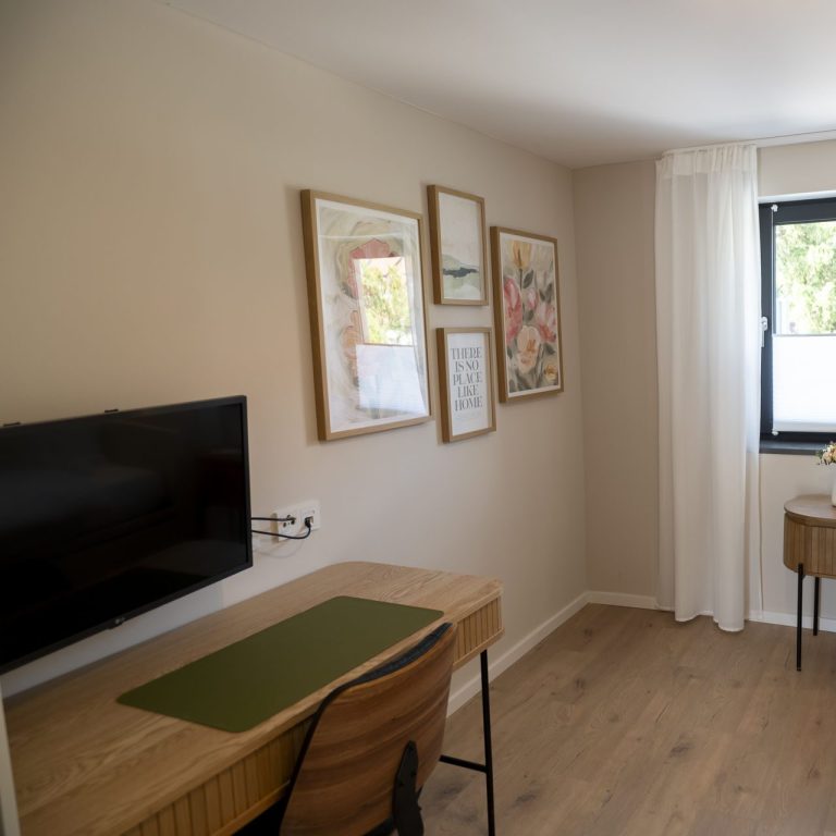 Schreibtisch Heller Raum mit Schreibtisch, Fernseher und blühenden Bildern an der Wand.