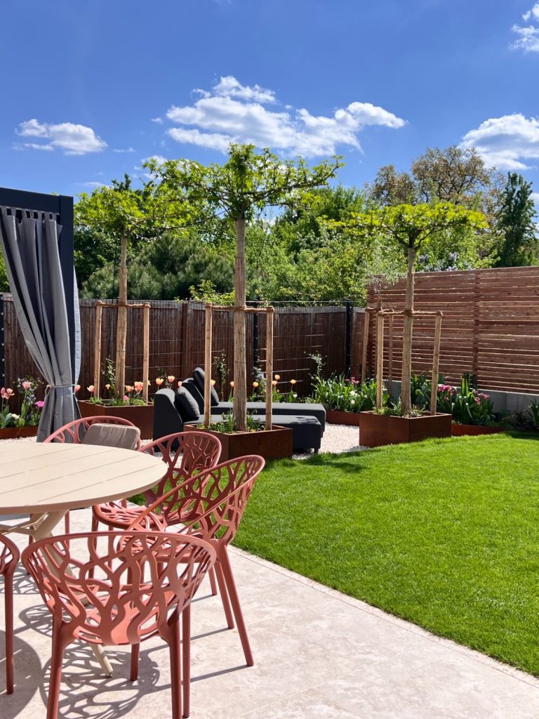 Garten mit grüner Rasenfläche, Gartenmöbeln und Bäumen unter blauem Himmel.