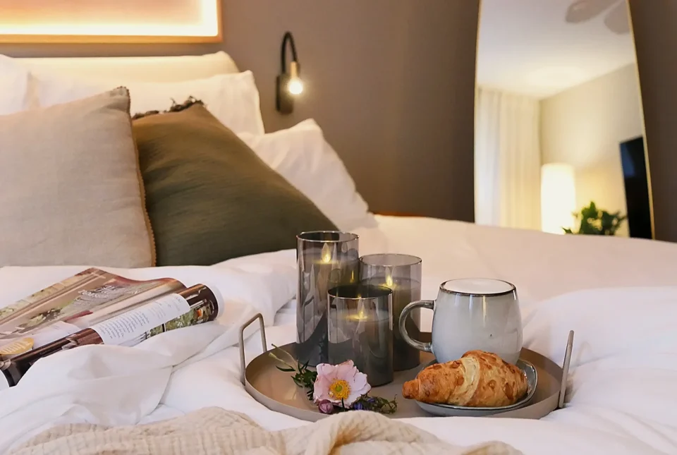 Frühstückstablett mit Kaffee, Croissant und Kerzen auf dem Bett