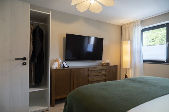 Bademäntel vorhanden Moderne Schlafzimmeransicht mit Fernseher, Kleiderschrank und sanfter Beleuchtung.