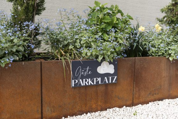 Blühende Pflanzen mit einem Schild "Parkplatz"