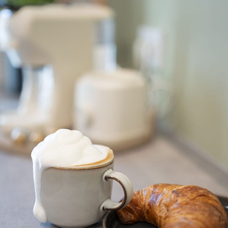 CoffeeTime Tasse mit Cappuccino und einem Croissant auf einem Tisch.