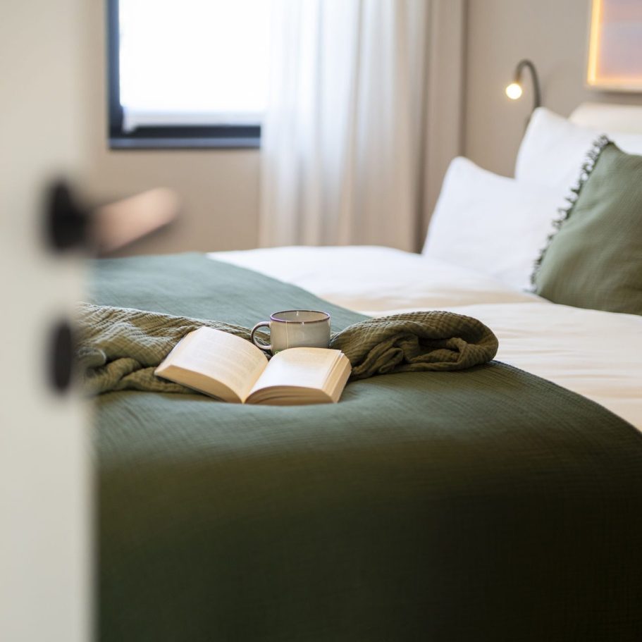GenussMoment Ein Schlafzimmer mit grüner Bettdecke, einem offenen Buch und einer Kerze.
