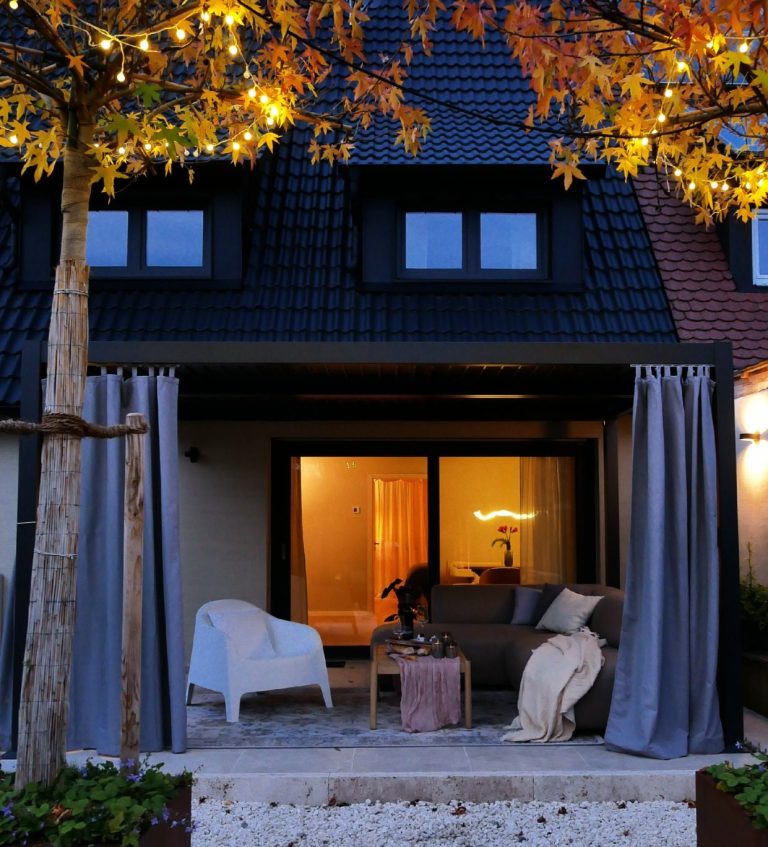 Terrasse Lounge Gemütlicher Außenbereich eines Hauses mit stimmungsvollem Licht und herbstlichen Blättern.