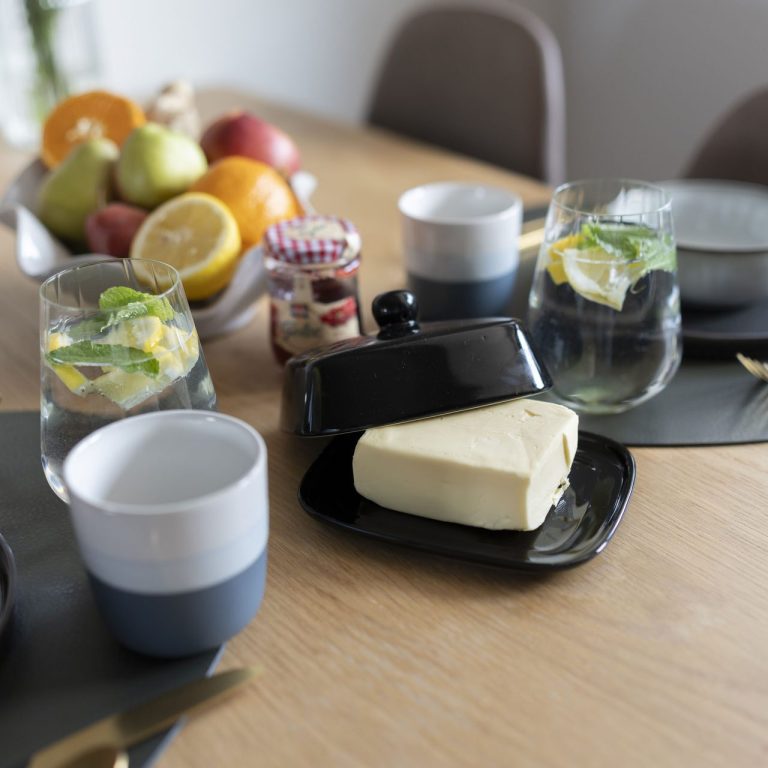 Frühstückzeit Ein gedeckter Tisch mit Obst, Gläsern, Tellern und Butter auf einem schwarzen Teller.