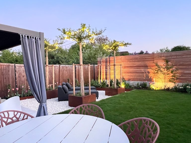 Heller Garten mit Sitzbereich, Bäumen und sanfter Beleuchtung am Abend.