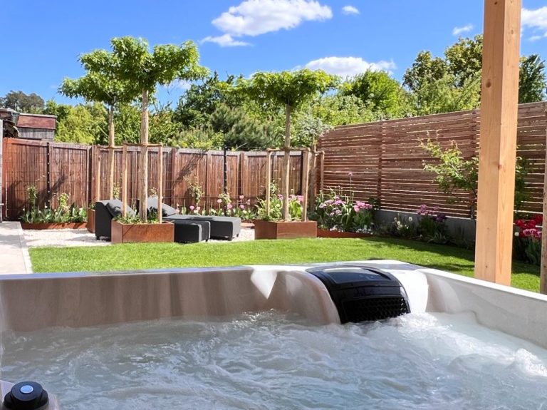 Moderner Garten mit Hot Tub, Rasenfläche und sanfter Beleuchtung am Abend.