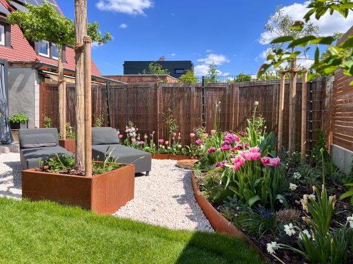 Garten mit blühenden Pflanzen, Sitzgelegenheiten und einem klaren blauen Himmel.