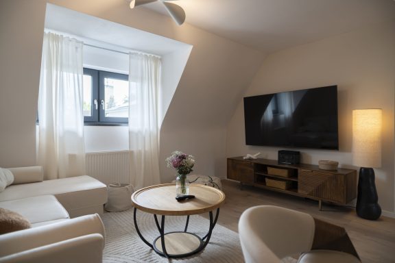 Fernseher mit Sky Heller Wohnraum mit Sofa, Tisch, Fernseher und einer Lampe neben einem Fenster.