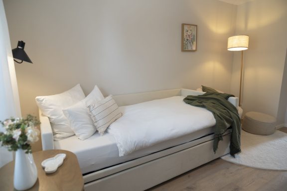 2. Schlafzimmer Helle, minimalistisch eingerichtete Ecke mit Bett, Kissen, Lampe und Pflanzen.